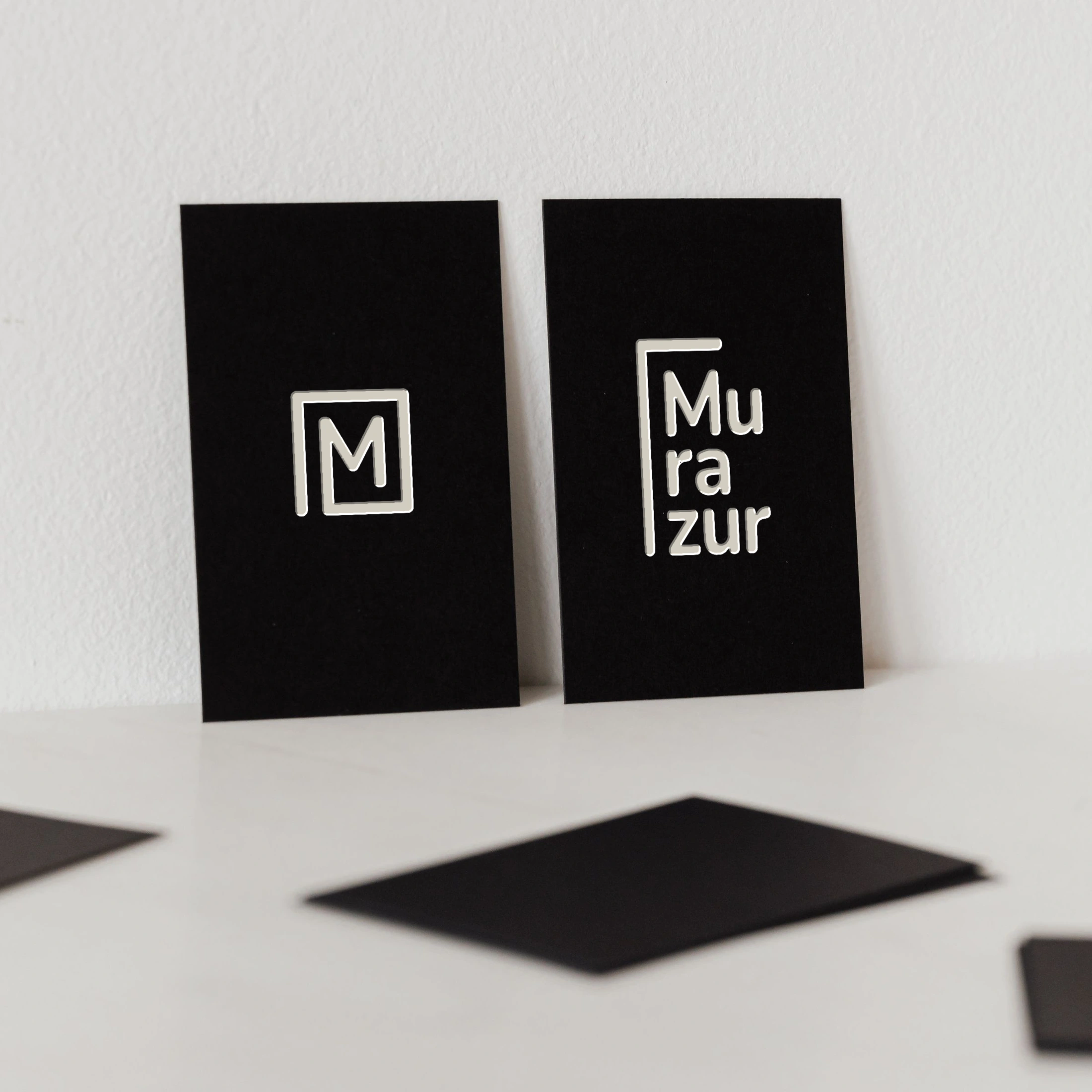 Tarjetas negras con el monograma y el logotipo vertical de Murazur